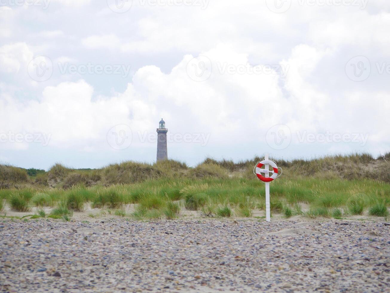 Red and white lifebuoy on the beach in Skagen, Denmark at the background of a lighthouse. Life saving rescue buoy. Lifeguard preserving concept photo
