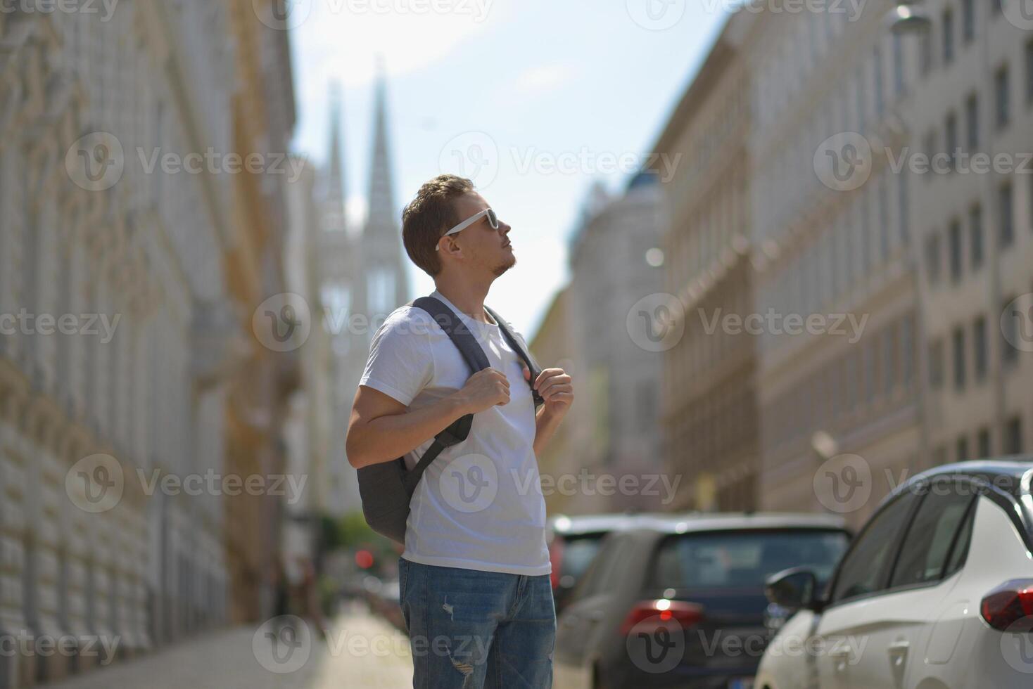 A man wearing white sunglasses and gray backpack on the street in Vienna on a hot sunny summer day. Tourism and sightseeing concept photo