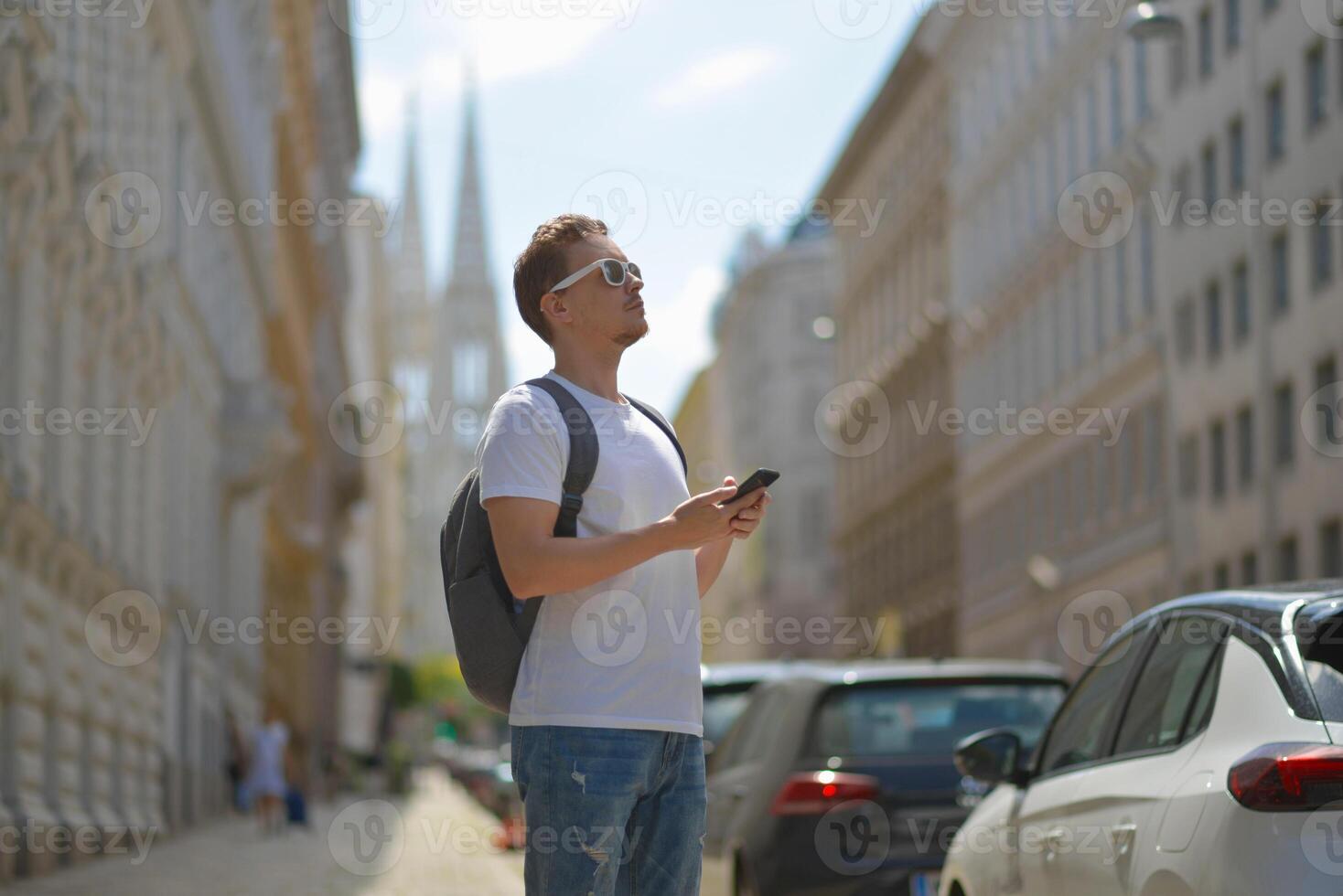 A man using smartphone wearing white sunglasses and gray backpack on the street in Vienna on a hot sunny summer day. Tourism and sightseeing concept photo