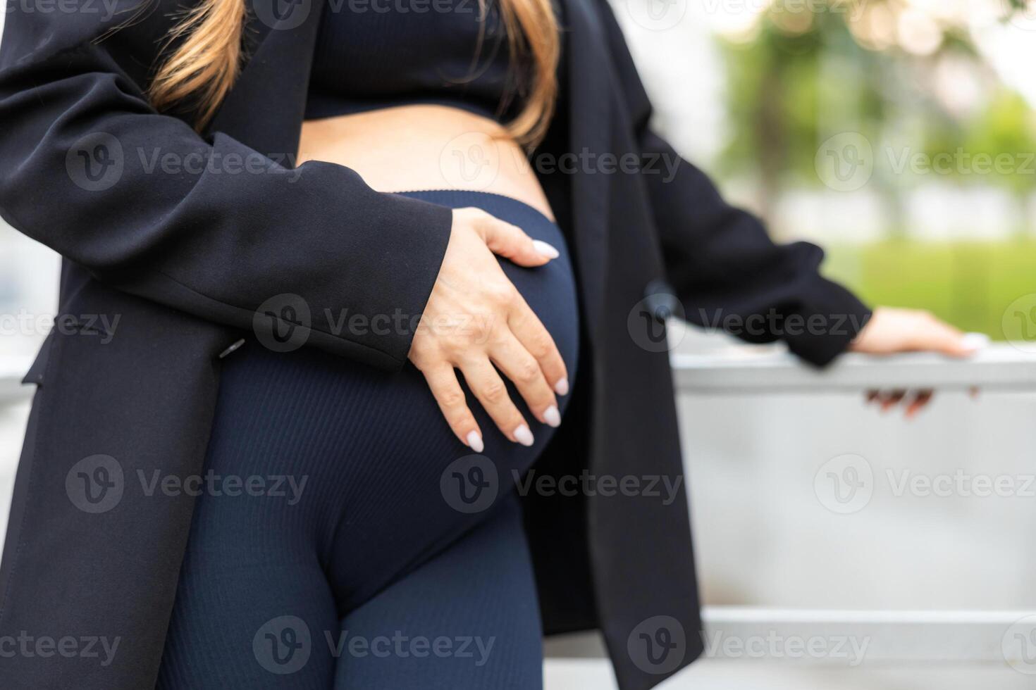 Close-up of torso of young pregnant model standing in park and caressing her belly. Concept future mom expecting baby photo