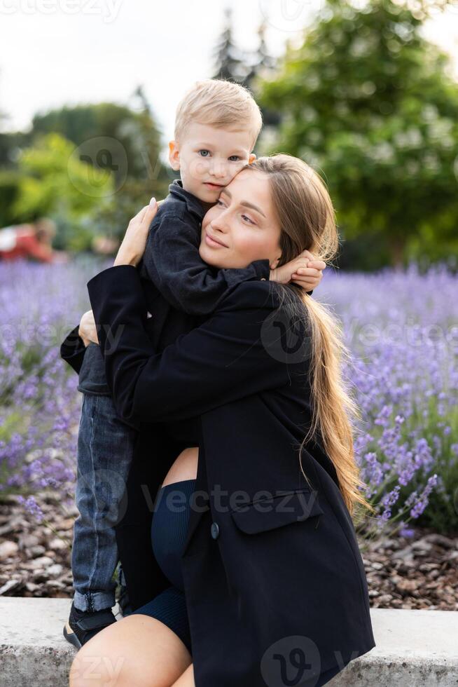 Pregnant mother and her little son spending time together in the park, hugging and smiling. photo