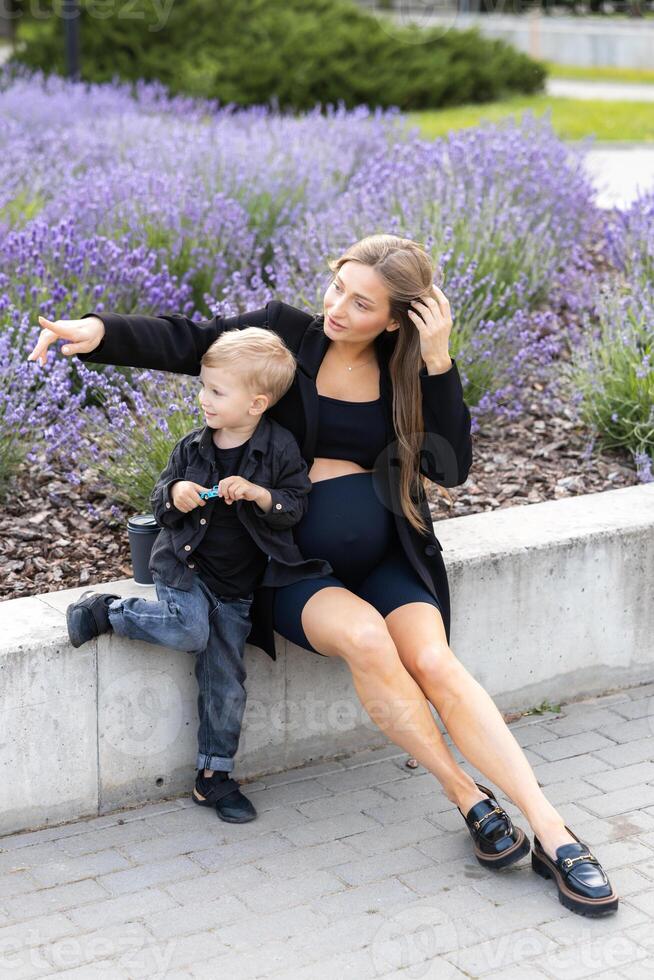 Pregnant mother and her little son spending time together in the park, hugging and smiling photo