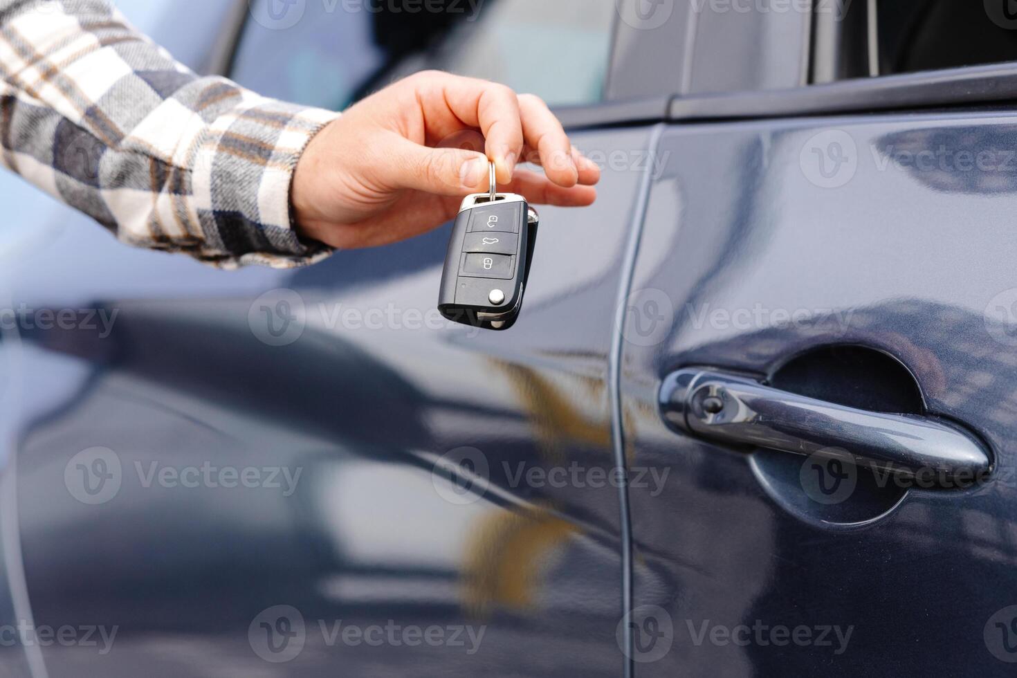 Emotional guy holding key in hand and smiling at camera. Man showing key from his new electric car. Young man buying auto at dealership salon photo