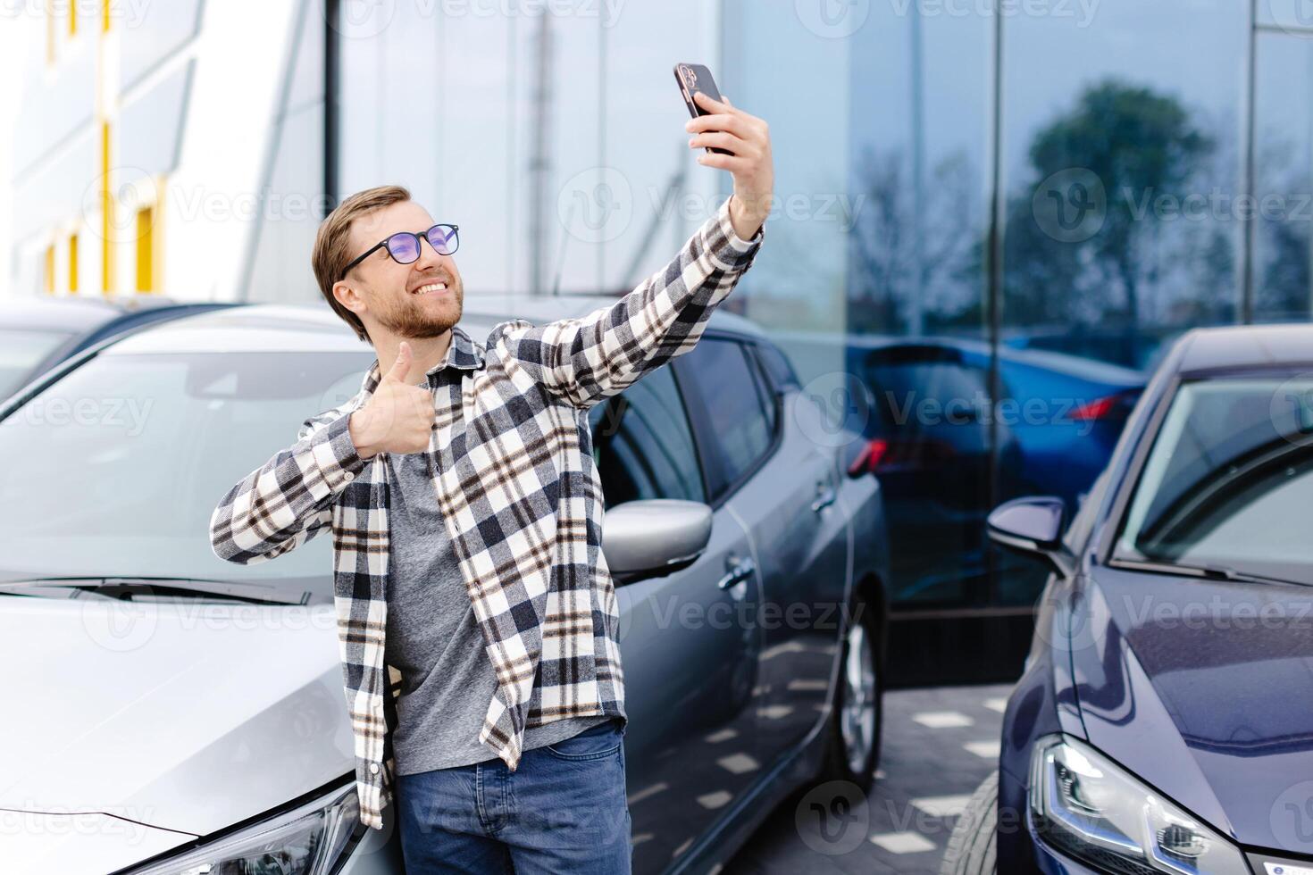 Happy man taking selfie through smart phone after purchasing new car. The man showing the purchased car via link over the phone photo