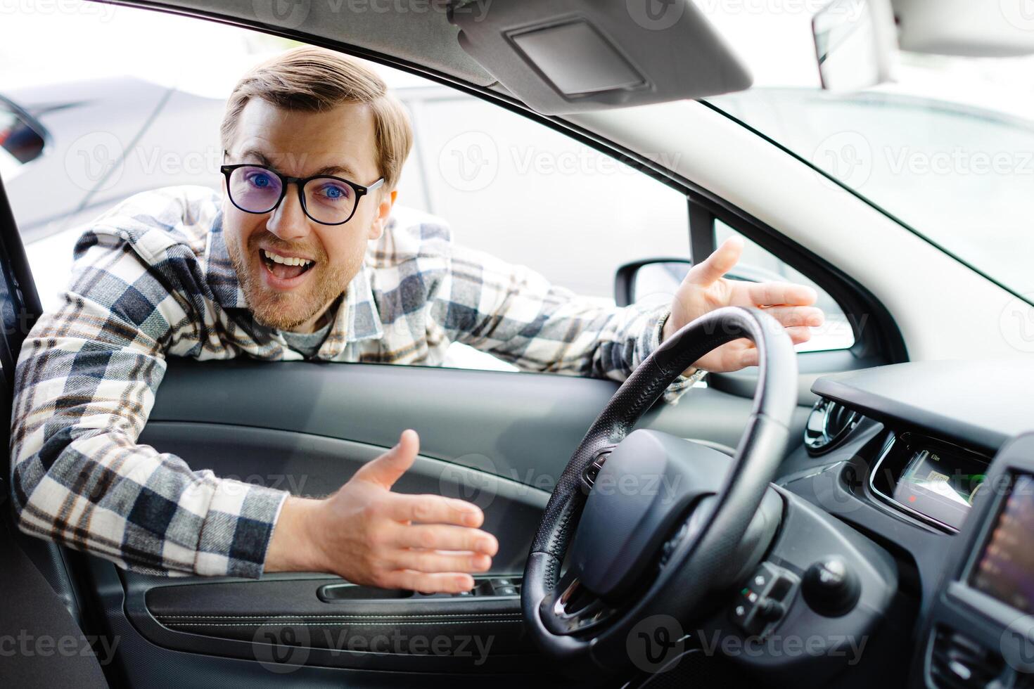 Young man looking through window inside new car, checking it before purchase at modern dealership store. Cheerful guy buying or renting automobile at showroom photo