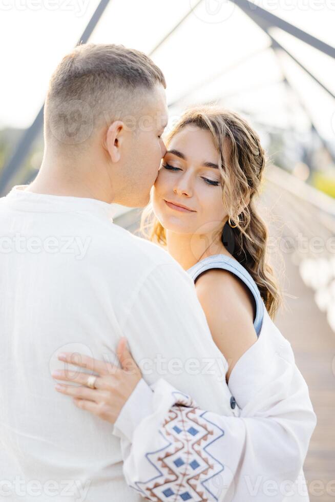 A Loving Couple Is Seen Embracing Each Other on a Beautiful Bridge on a Sunny Day, Surrounded by the Warmth of the Sun photo