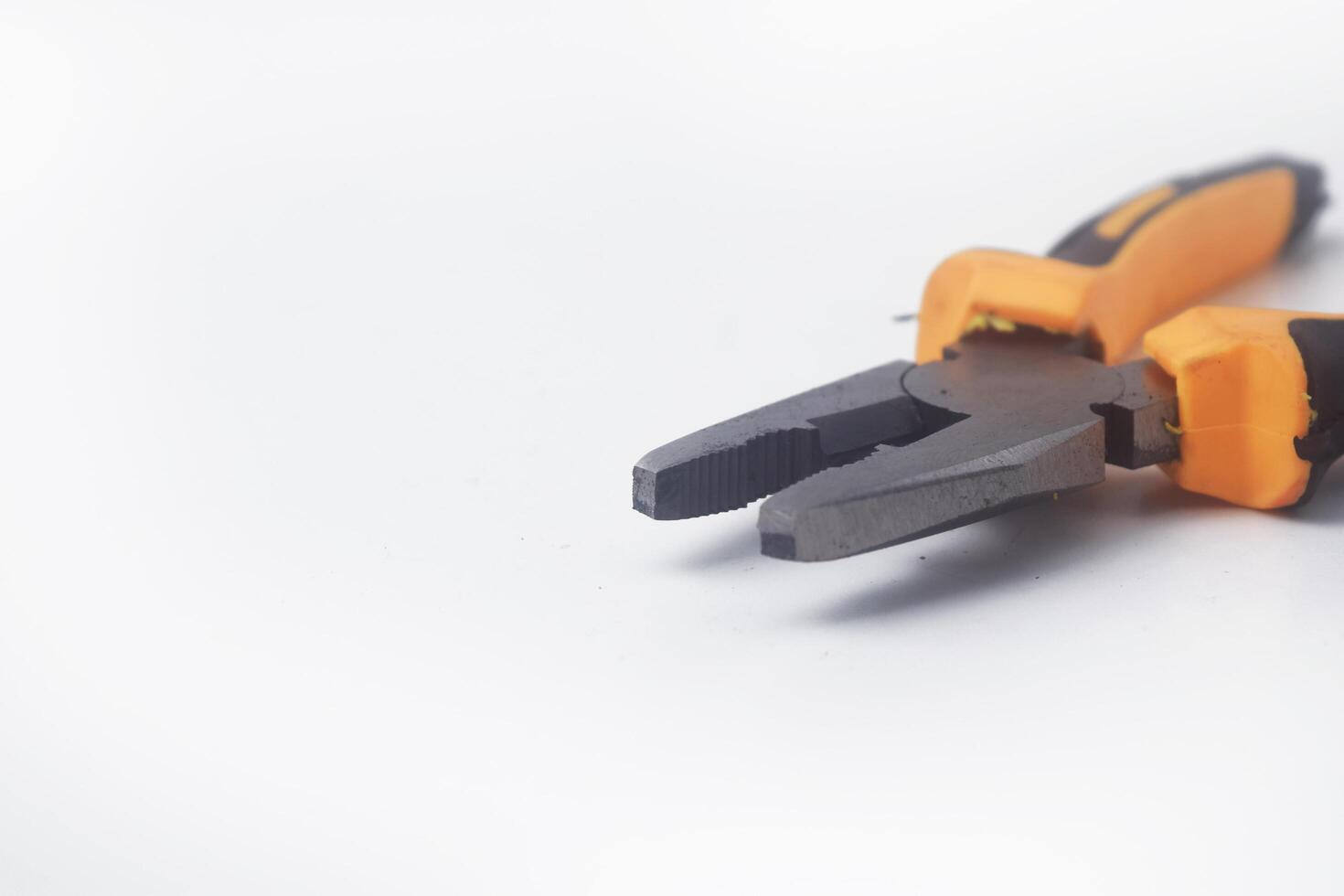 Closeup photo of a pair of pliers with a yellow handle on a white background
