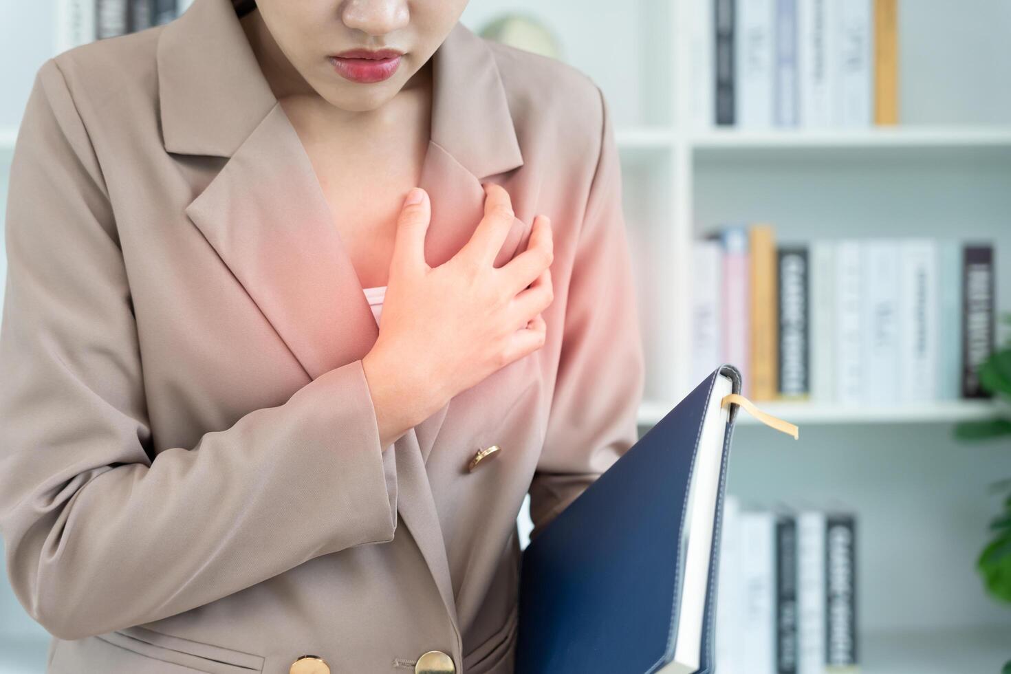 hand hold chest with heart attack symptoms, asian woman working hard have chest pain caused by heart disease, leak, dilatation, enlarged coronary heart, press on the chest with painful expression photo