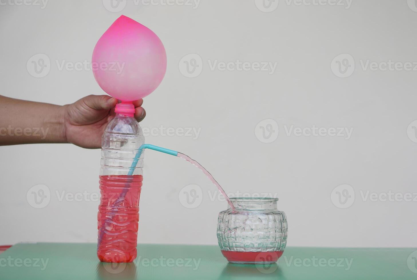 Science experiment with air in pink balloon on the top of bottle with red water and straw tube to put water flow into glass jar. Concept, teaching aids, educational materials. Creative science lesson. photo