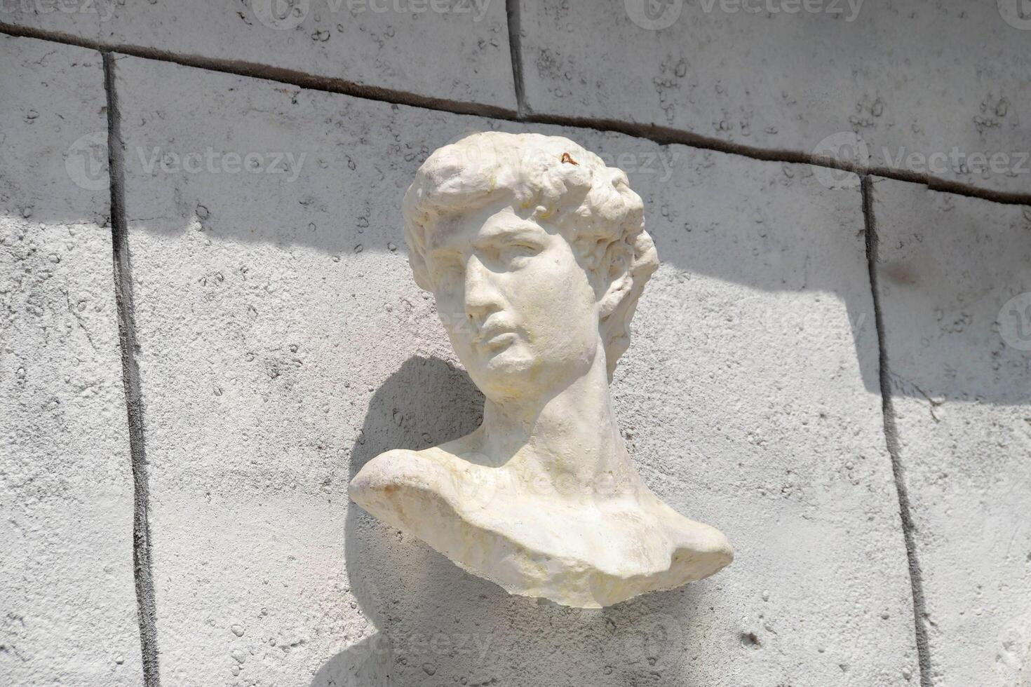 A sculpture of a mans head displayed against a white wall photo