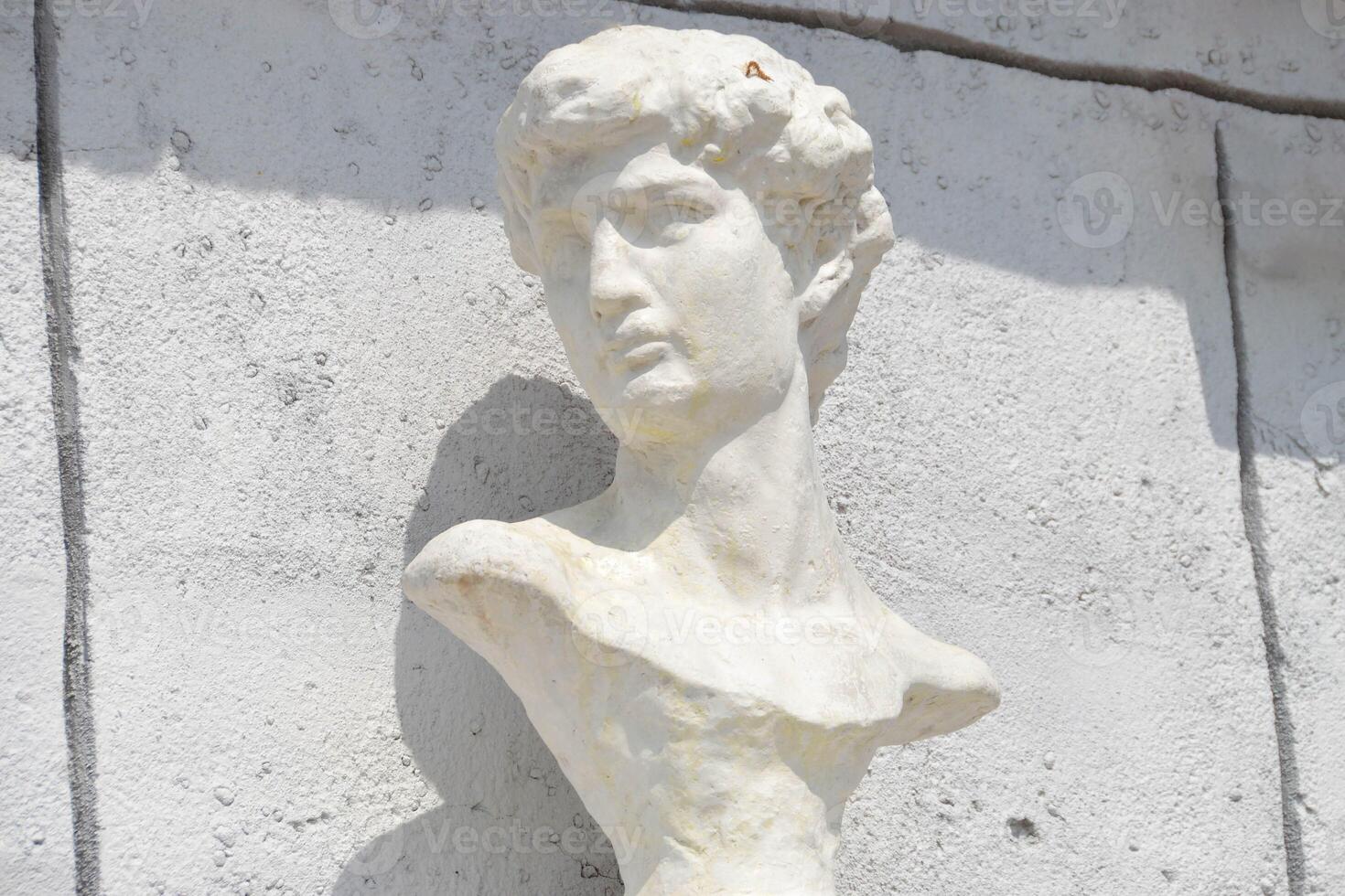 A sculpture of a mans head displayed against a white wall photo
