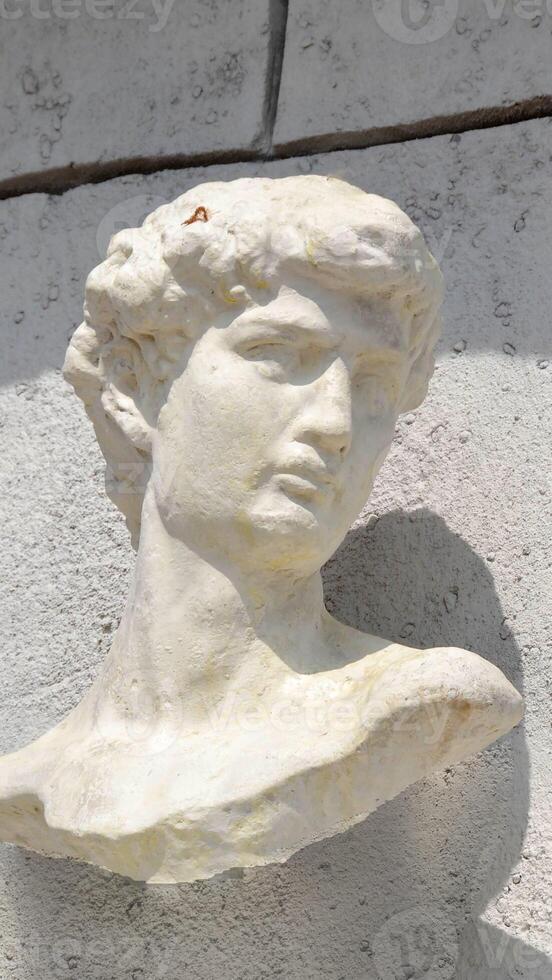 A sculpture of a mans head displayed against a white wall photo