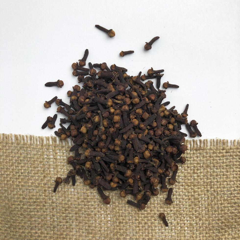 Pile of cloves spice isolated on burlap fabric and white background. The view from top. photo