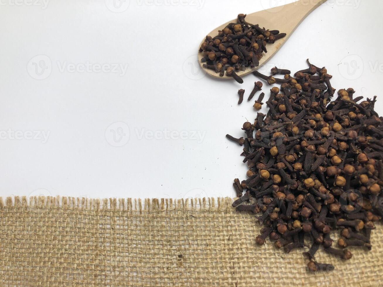 Pile of cloves spice with wooden spoon isolated on burlap fabric and white background. photo