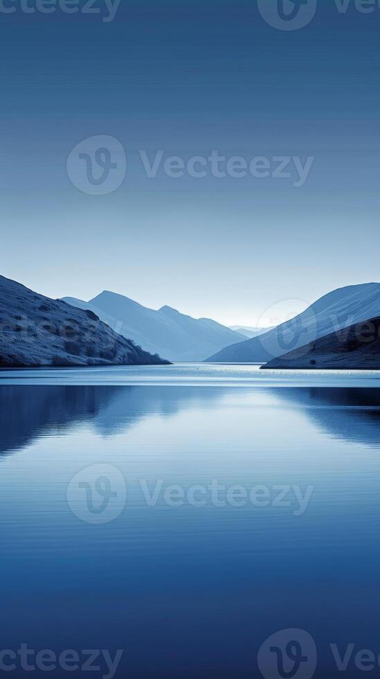 A still lake reflecting a mountain range under a clear, blue sky photo