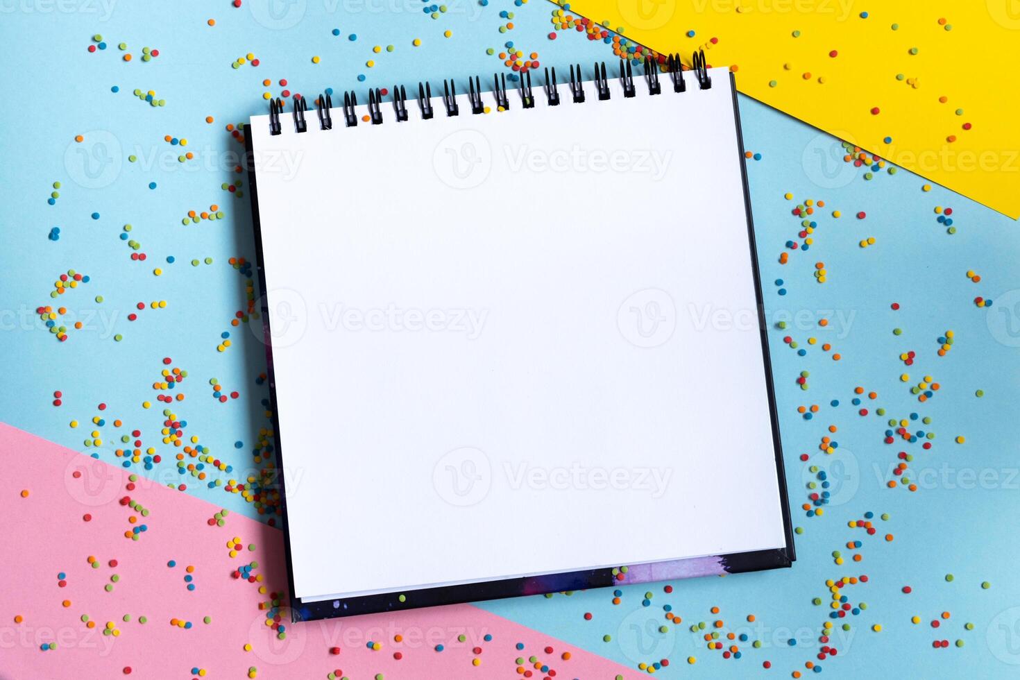 Mock up of empty spiral scketchbook with white paper on bright vibrant background with colorful confetti . Copy space. photo