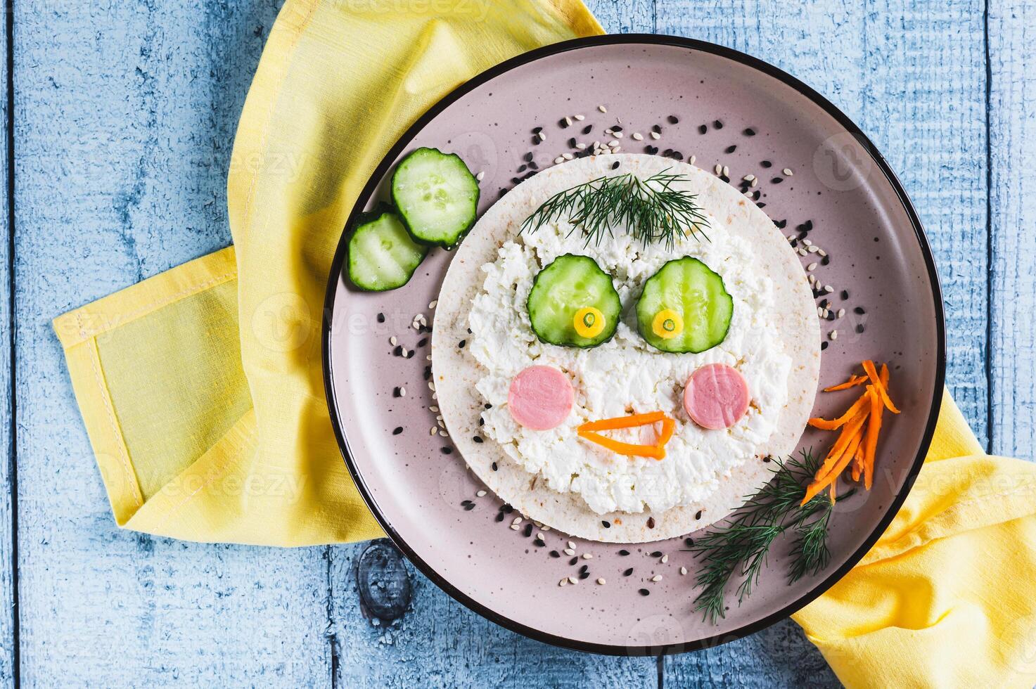 Close up of face made of tortilla, ricotta, sausages, vegetables for children's breakfast top view photo