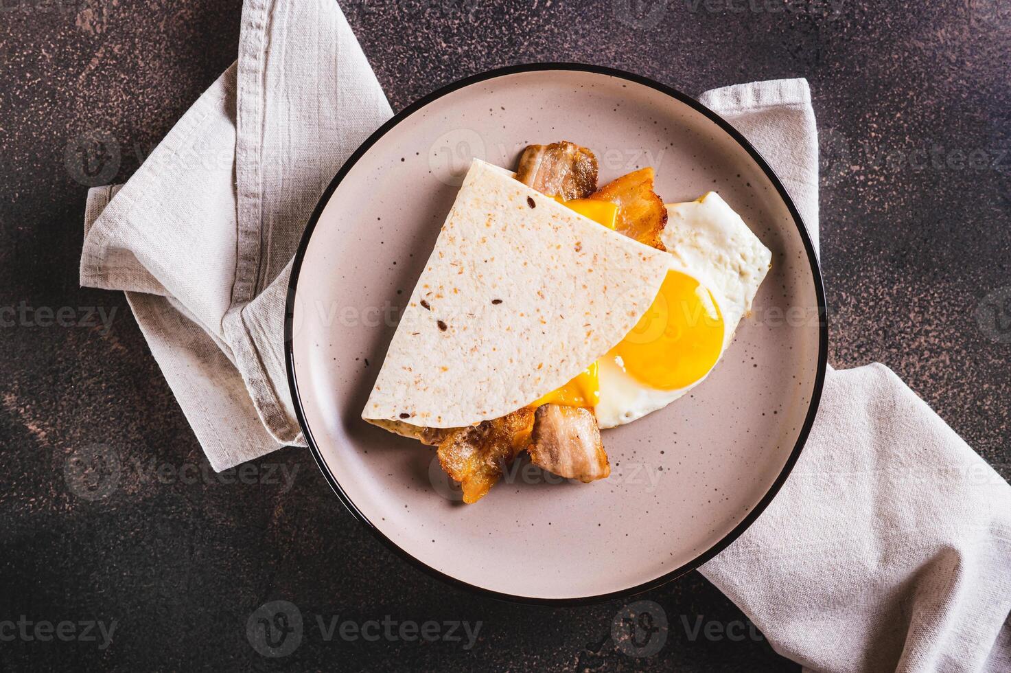 Close up of quesadilla with fried egg, bacon and cheese on a plate on the table top view photo