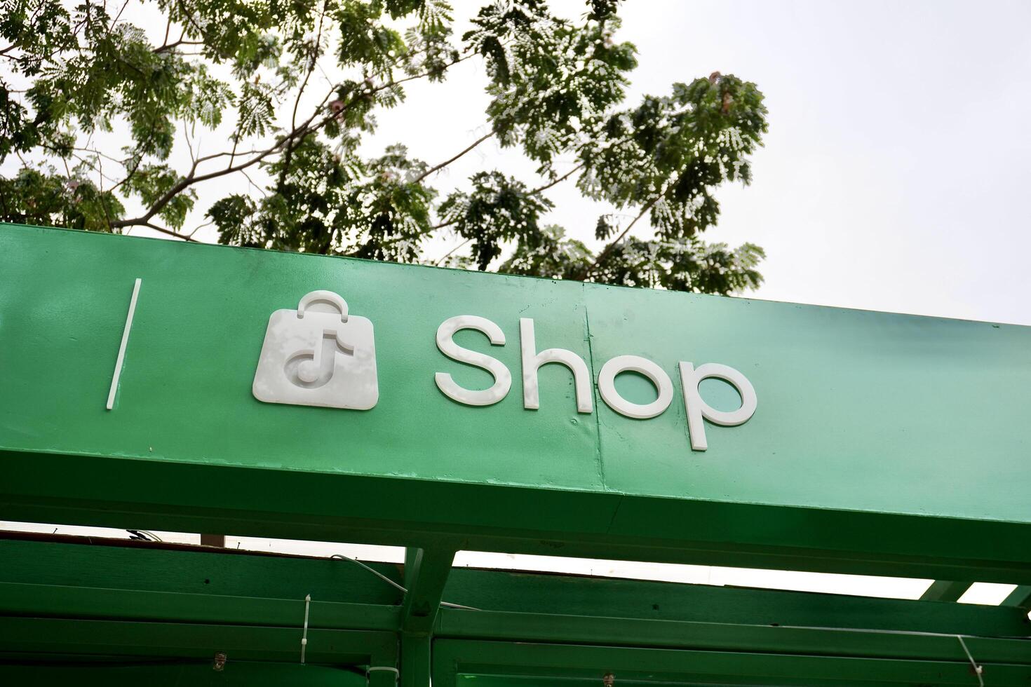 Jakarta, Indonesia - July 27th, 2024 - Tiktok shop brand logo sign banner on green building exterior structure isolated on horizontal outdoor bright sky and green tree background. photo