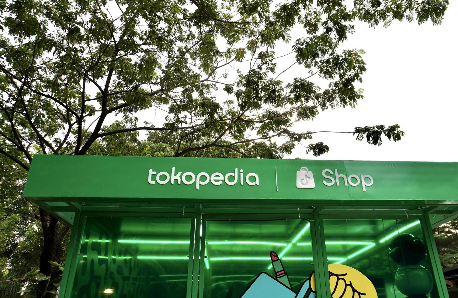 Jakarta, Indonesia - July 27th, 2024 - Tiktok shop and tokopedia brand logo sign banner on green building exterior structure isolated on horizontal outdoor bright sky and green tree background. photo