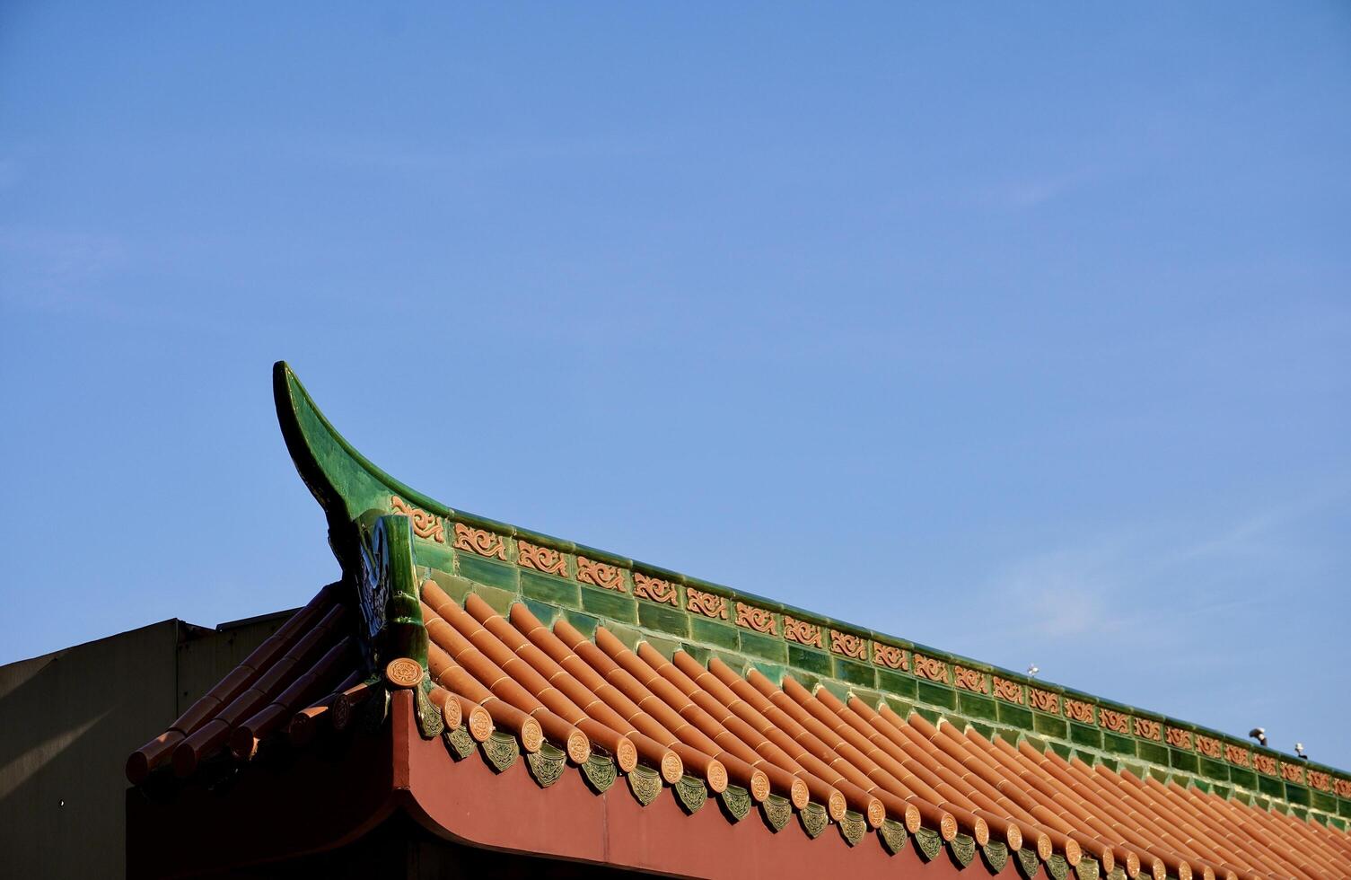 Brown and green building roof with chinese styled architecture design isolated on horizontal bright blue sky empty copy spaced background. photo