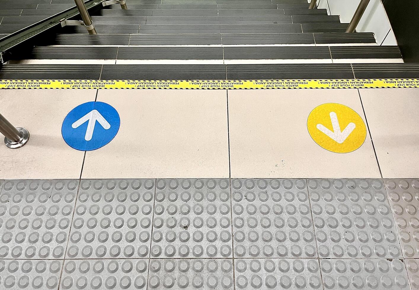 Blue and yellow colored go up and down arrow direction stickers on horizontal train station stair way path flooring and braille block pavement background. photo