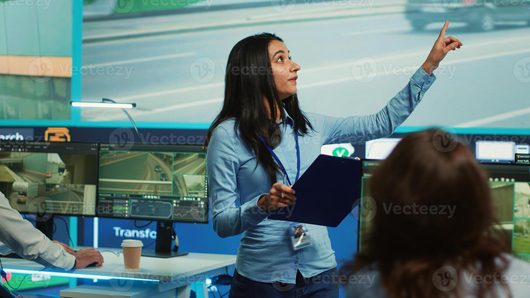 Indian supervisor assigning tasks for her operators team in observation room, people monitoring traffic through surveillance CCTV footage. Agency using satellite radar for public safety. Camera A. photo