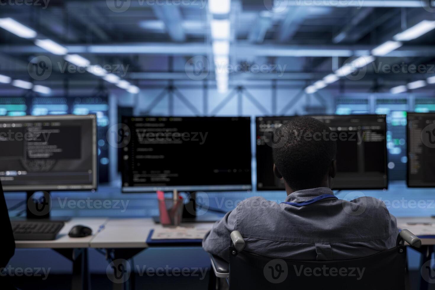 Person with disability in inclusive server hub workspace ensuring data remains shielded from threats. African american wheelchair user safeguarding data center establishment infrastructure photo
