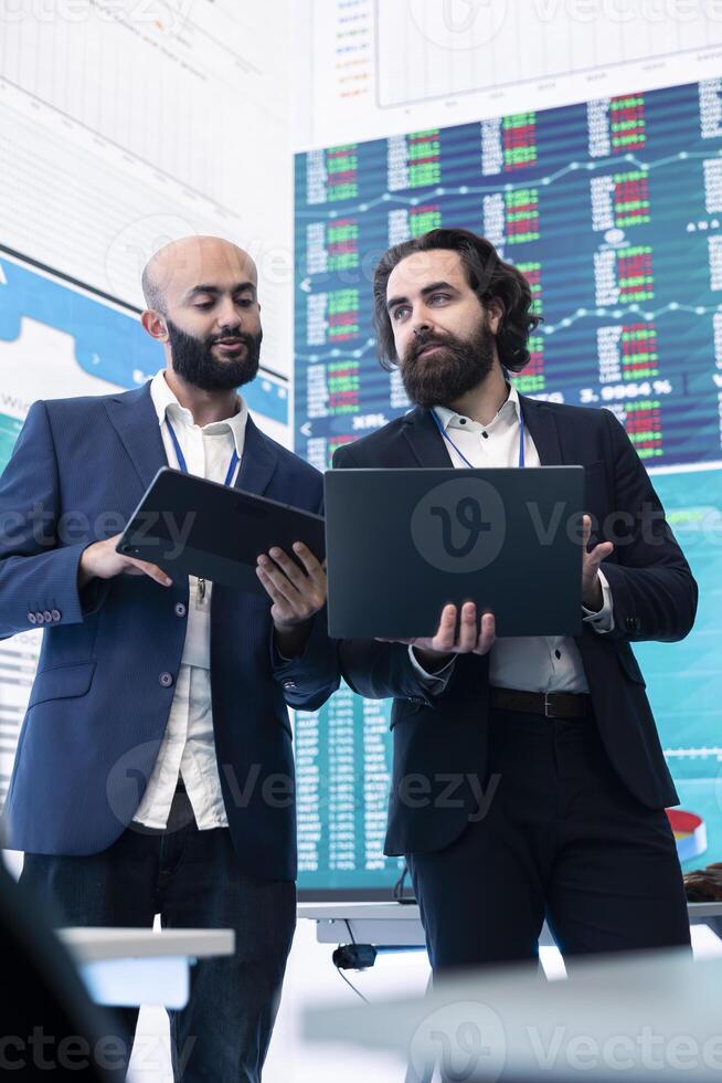 Diverse group of business specialists solve their daily tasks in control room with big screen, analyzing data numbers to ensure organizational progress. Startup management team. photo