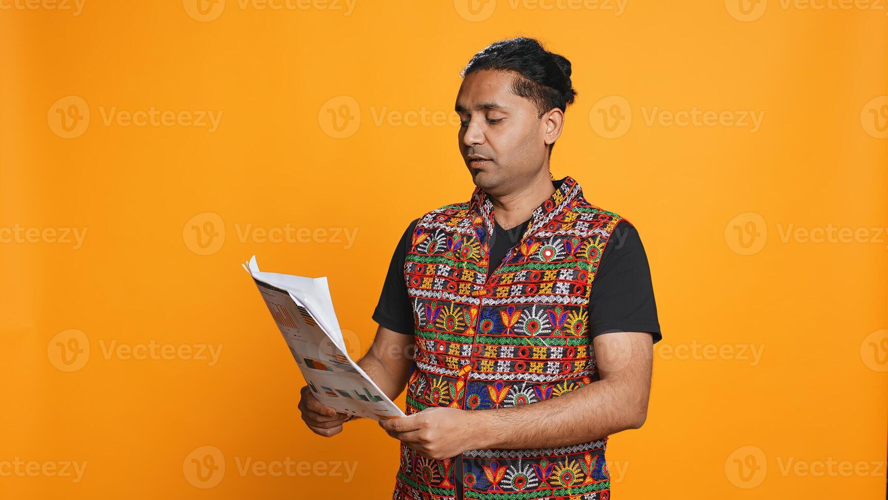 Man browsing though financial audit report files, slapping them in anger, disappointed by results, studio background. Upset indian worker frowning, annoyed by paperwork, camera B photo