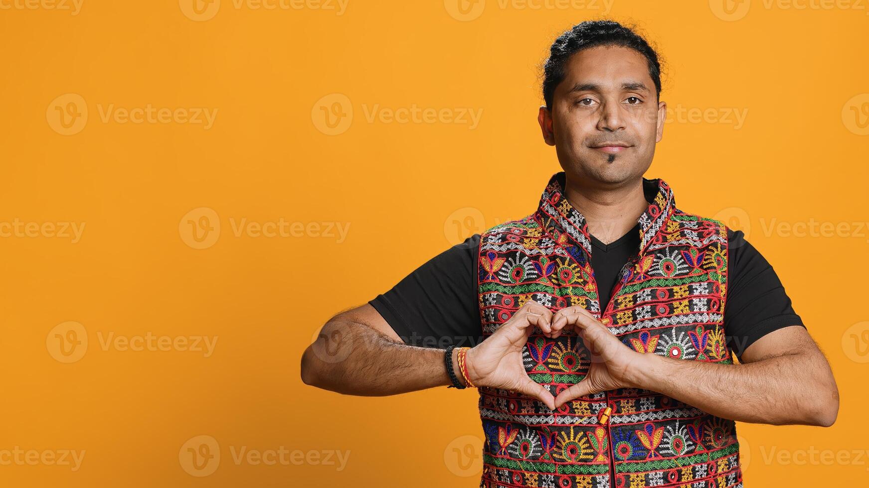 Portrait of smiling loving man doing heart symbol shape gesture with hands, showing kindness. Happy affectionate person doing tender love gesturing, isolated over studio background, camera A photo