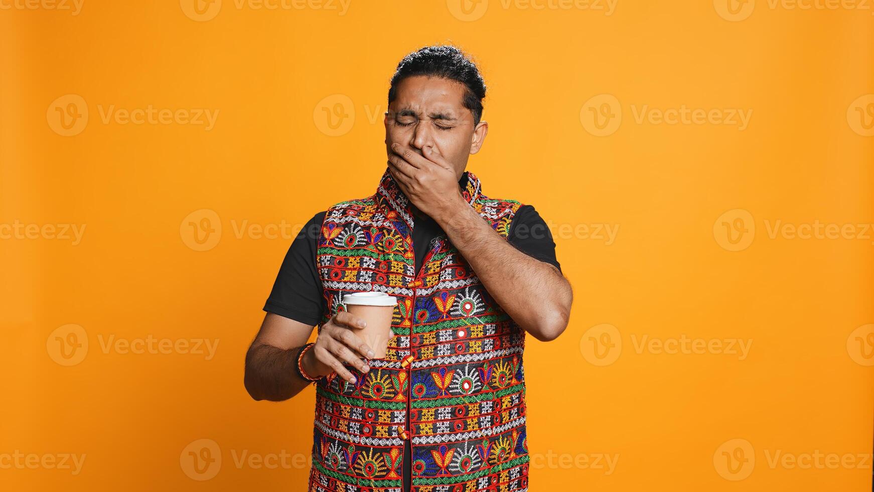 Tired indian man sipping fresh coffee from disposable paper cup early in the morning to wake up and be energized. Person drinking hot beverage from recycled takeaway cup, studio background, camera B photo