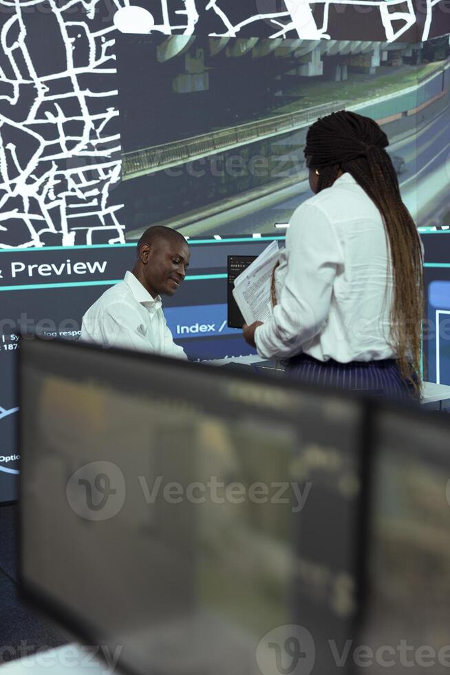 African american team studies order tracking logistics and gps coordinates of the delivery location, using CCTV surveillance footage and satellite navigation in agency headquarters. photo