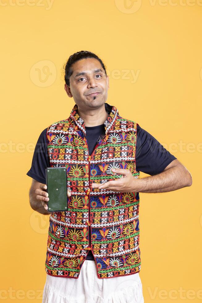 Upbeat influencer presenting green screen mobile phone, isolated over studio background. Indian person holding copy space chroma key smartphone used for advertising brands photo