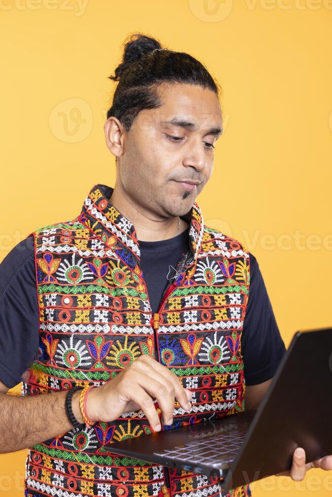 Indian man composing email, typing on laptop, frustrated with malfunctioning keyboard. Person sending mail online, struggling to use defective notebook, studio background photo