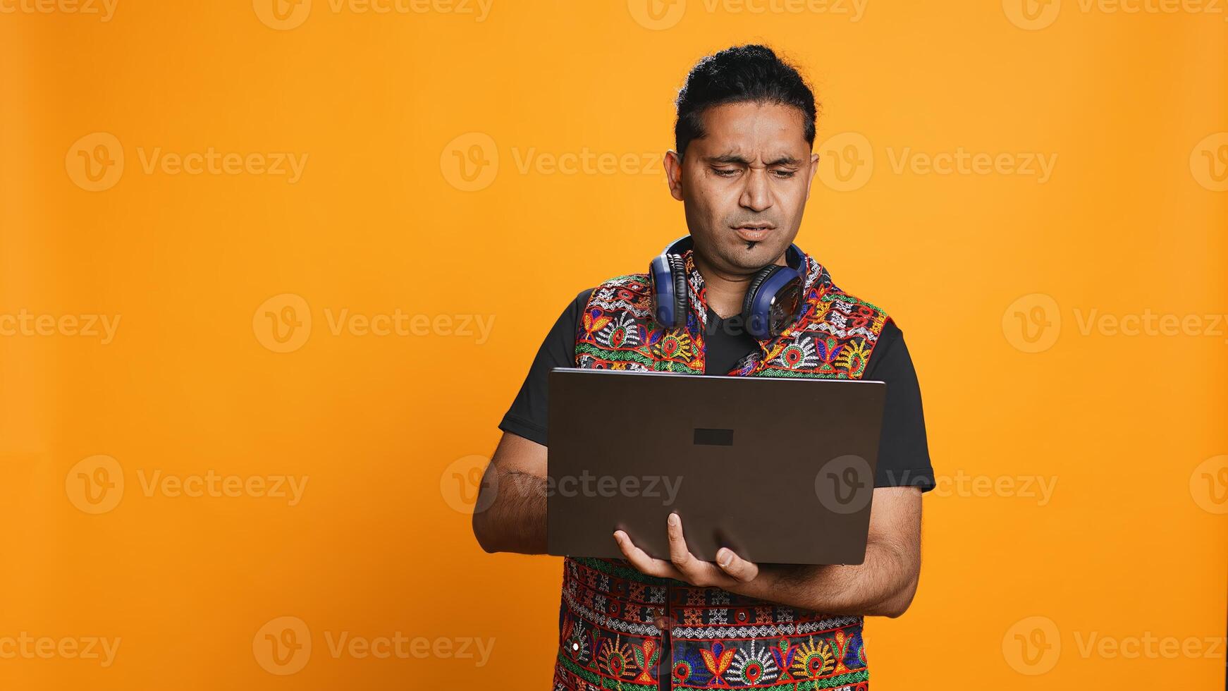 Indian man composing email, typing on laptop, frustrated with malfunctioning keyboard. Person sending mail online, struggling to use defective notebook, studio background, camera B photo