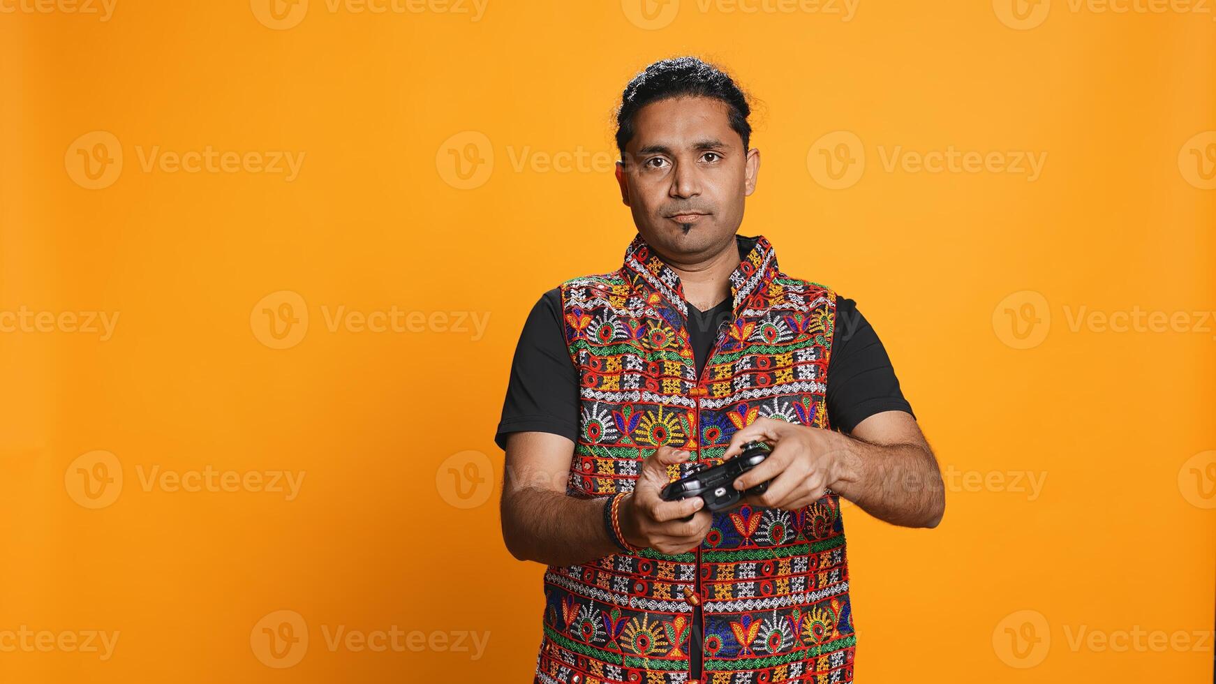 Upset man showing thumbs down sign gesturing holding controller, disapproving of videogames. Displeased indian person against gaming, doing rejection hand gesture, studio background, camera B photo