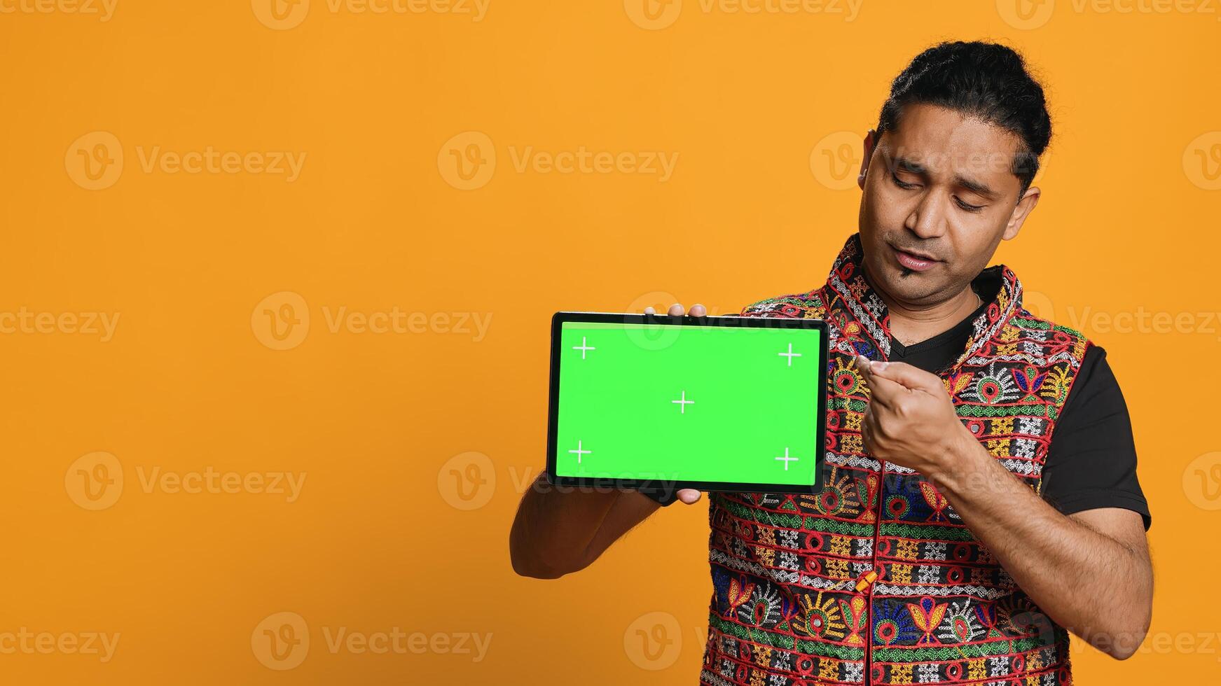 Portrait of indian man doing influencer marketing using green screen tablet, isolated over studio background. Smiling person holding empty copy space mockup device, camera A photo