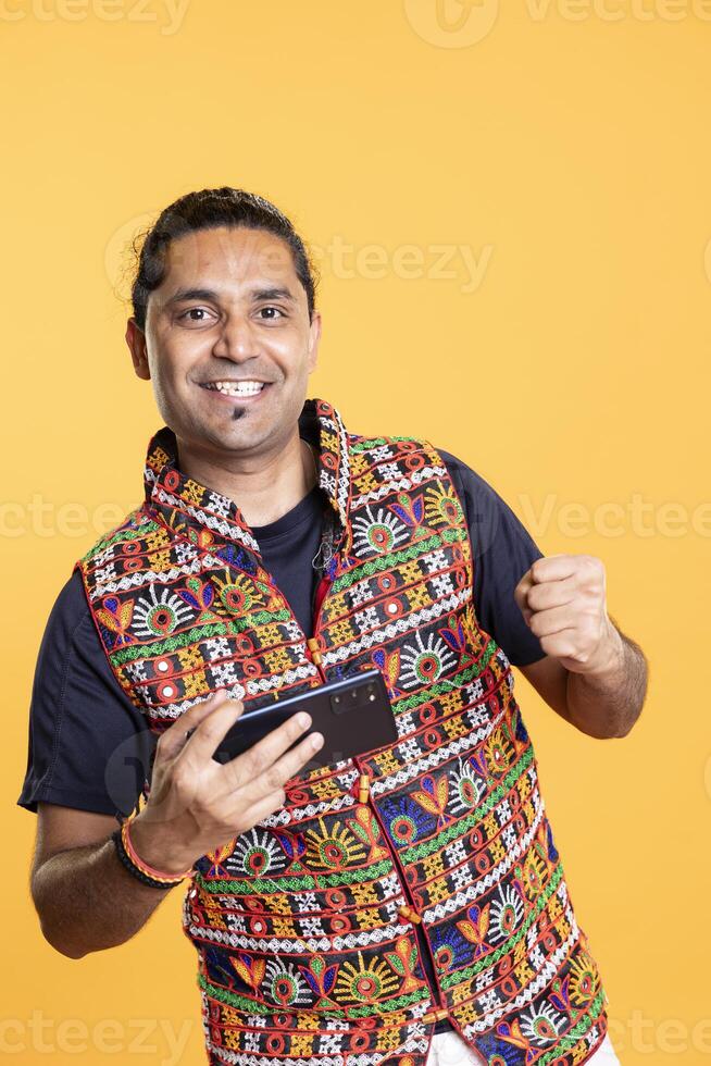 Overjoyed player celebrating after winning game on cellphone, studio background. Euphoric gamer bragging after being victorious in videogame, defeating all enemies on mobile phone photo