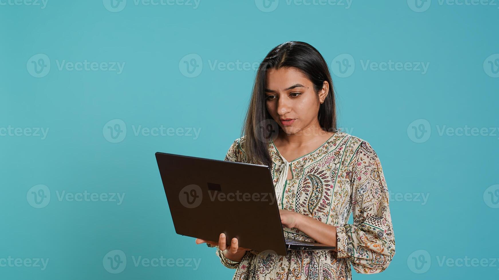 Indian woman composing email, typing on laptop, frustrated with malfunctioning keyboard. Person sending mail online, struggling to use defective notebook, studio background, camera A photo