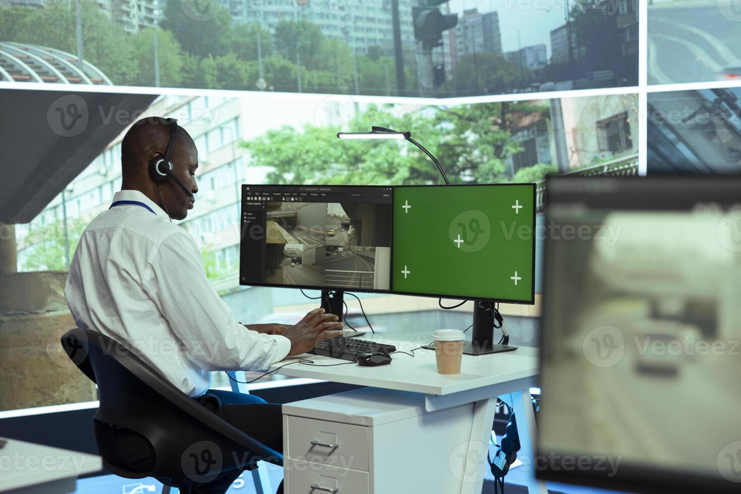 African american operator monitoring traffic through CCTV surveillance next to a greenscreen display, security cameras footage at stop lights. Employee gathering data on cars via satellite. photo