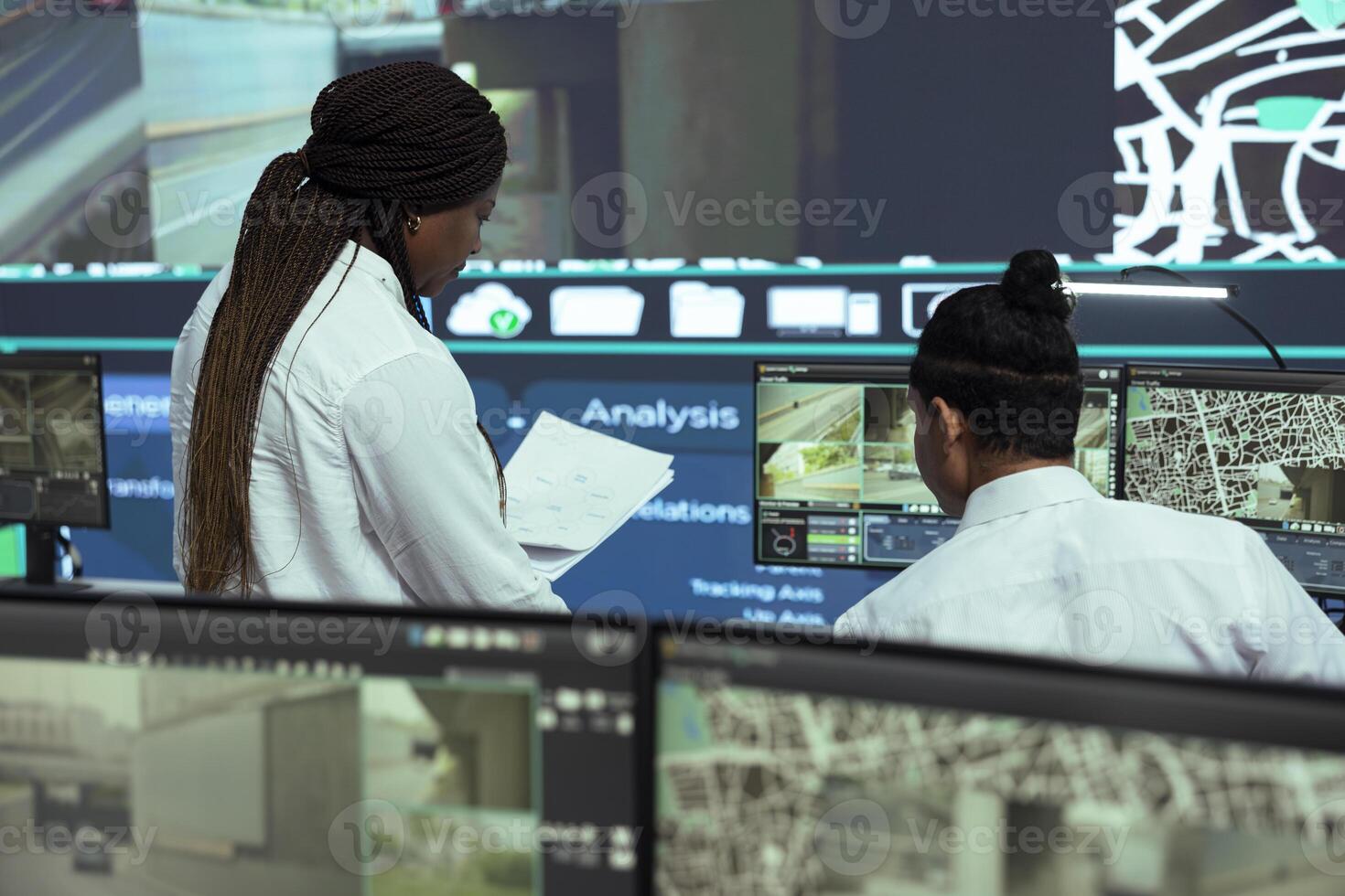 Manager offers logistics papers to indian employee in observation room, following delivery trucks on satellite navigation for routes around the city. Worker operating on CCTV public system. photo