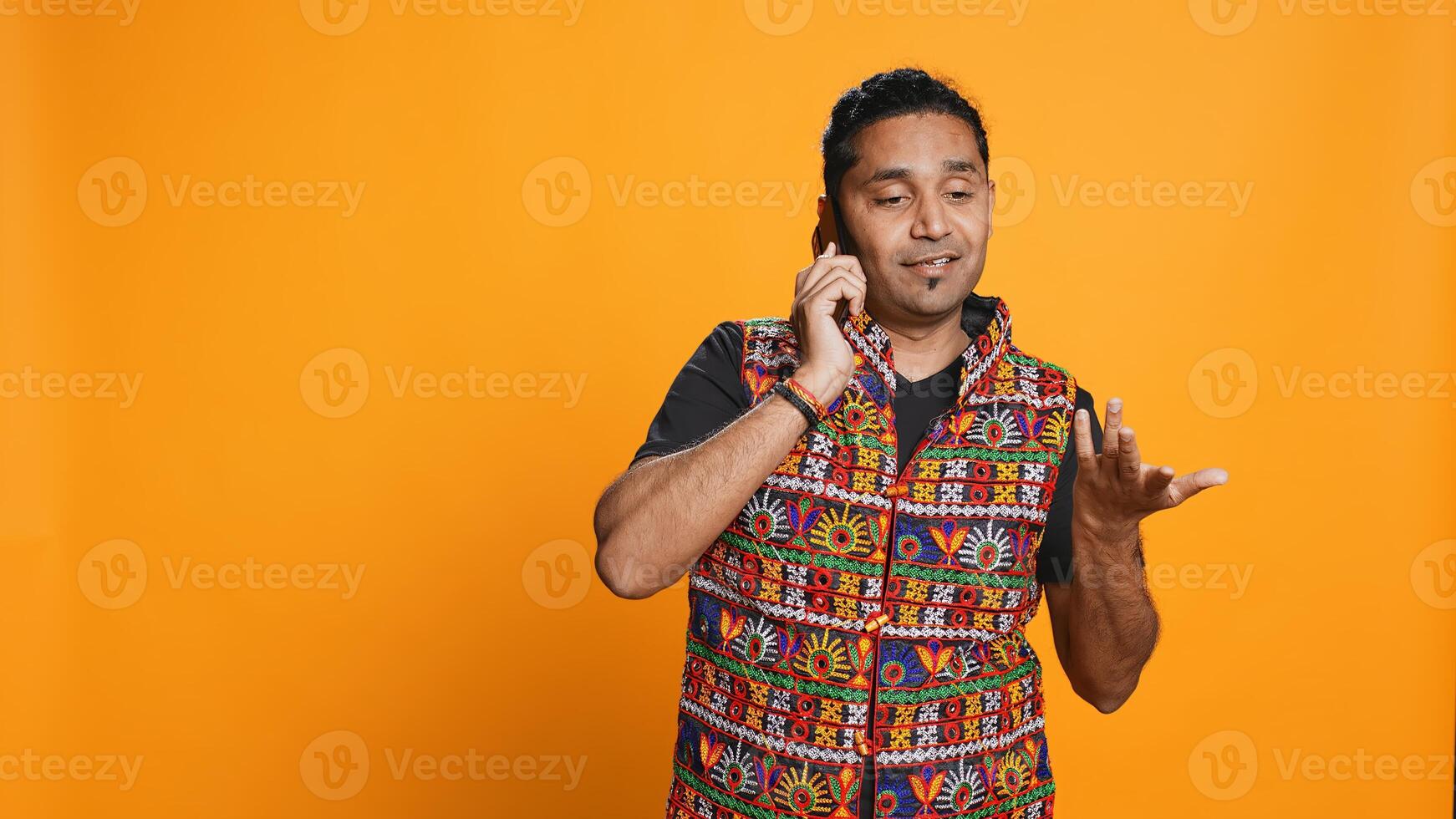 Man discussing with best friend over telephone call, enjoying leisure time. Upbeat person wearing indian attire talking with mate in phone call, isolated over studio backdrop, camera B photo