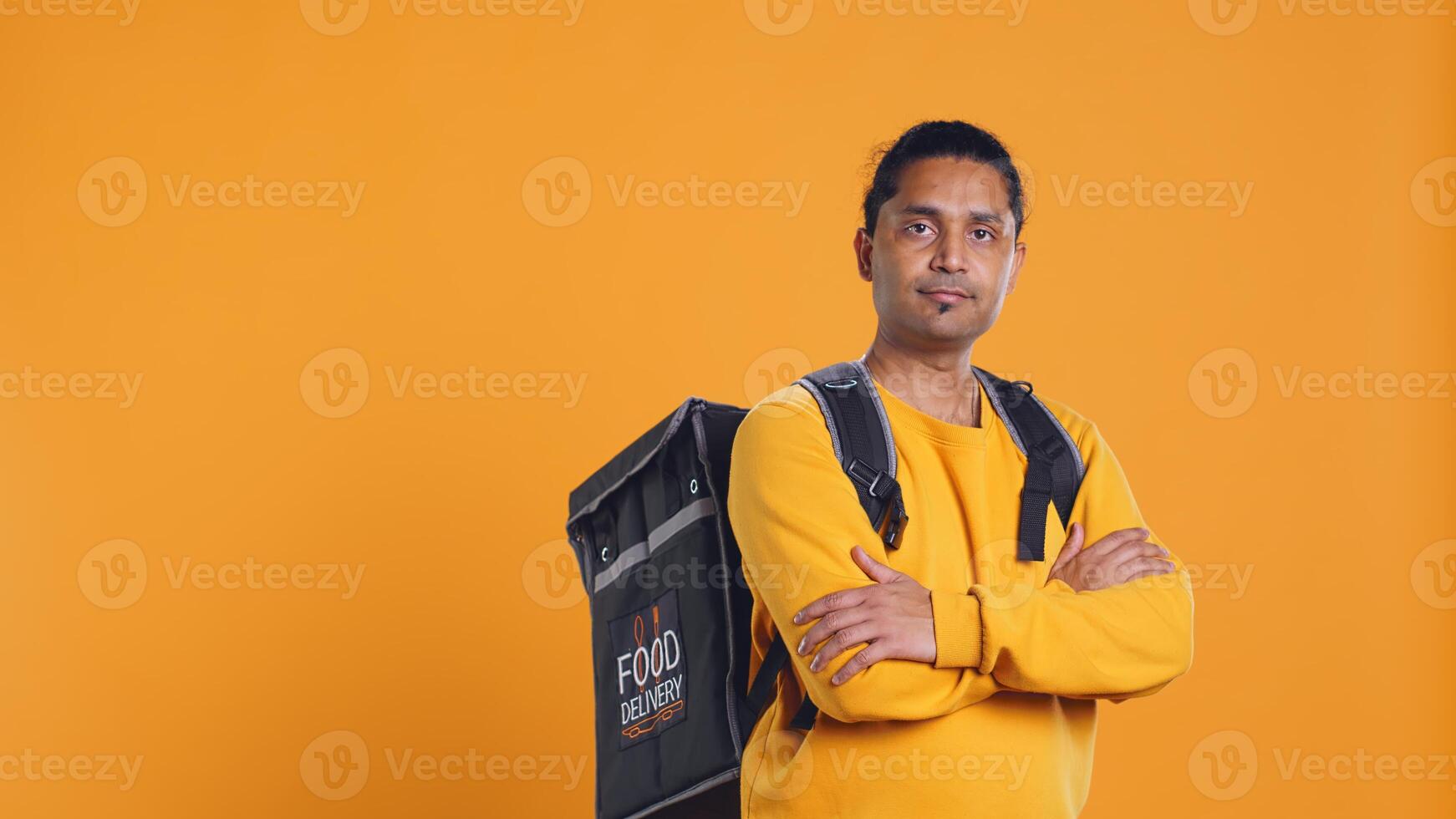 Portrait of upbeat indian man holding thermal backpack, isolated over studio background. Friendly cheerful person prepared to deliver takeaway food to customers, camera B photo