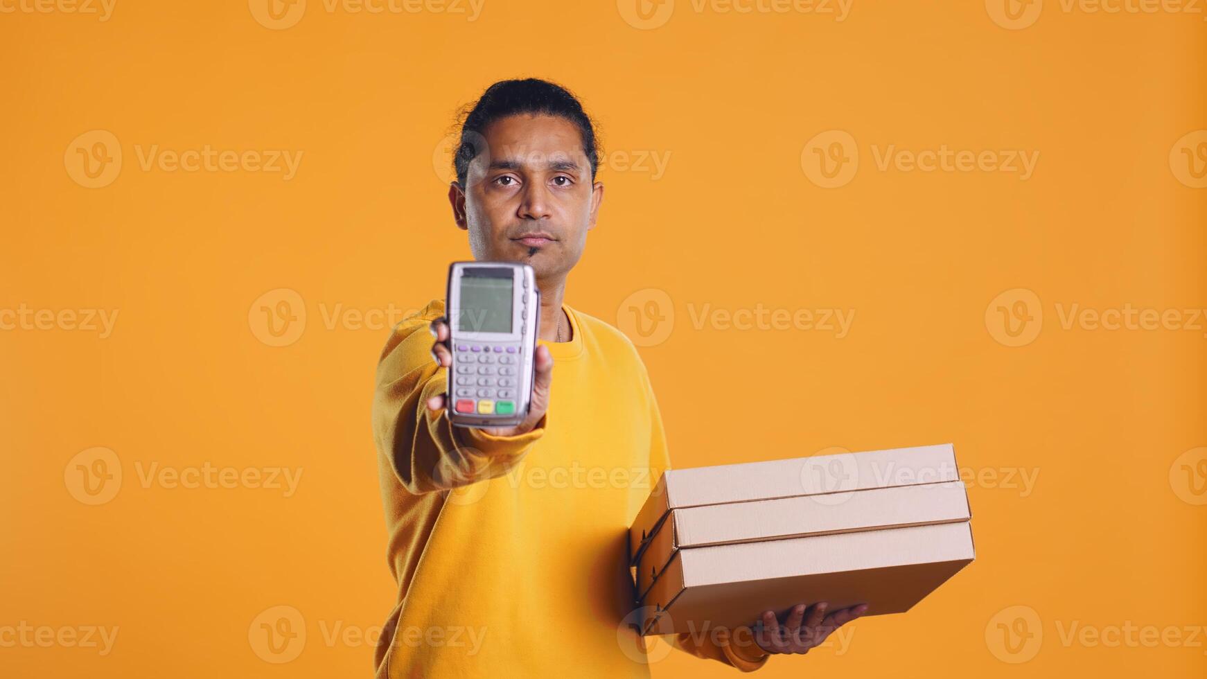 Portrait of courier isolated over studio background carrying stack of pizza boxes, close up shot. Indian employee delivering food waiting for client to answer door and pick up meal order, camera B photo