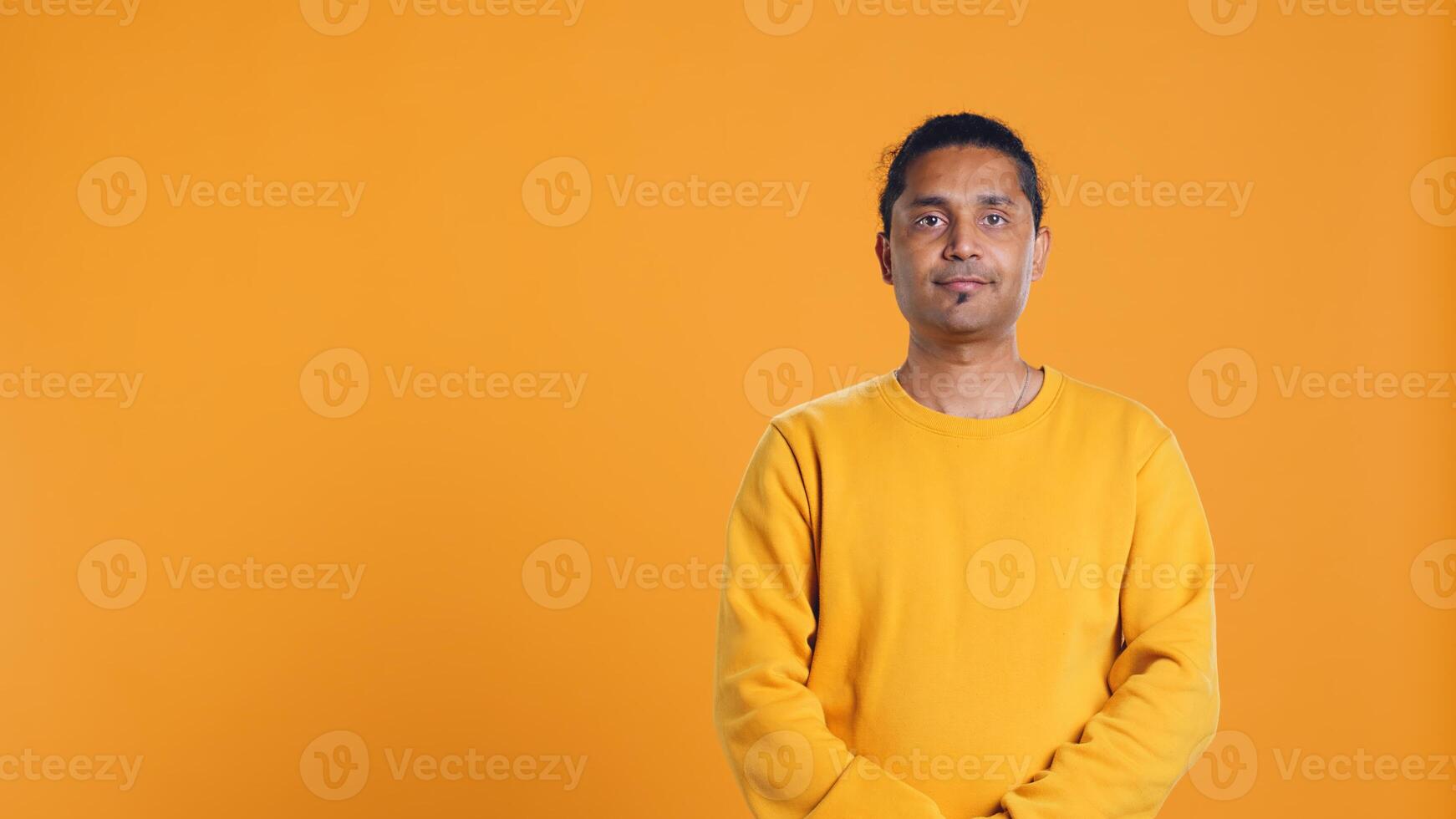 Portrait of radiant optimistic indian man with positive facial expression smiling, looking pleased. Calm merry person crossing arms, feeling satisfied, studio backdrop, camera B photo