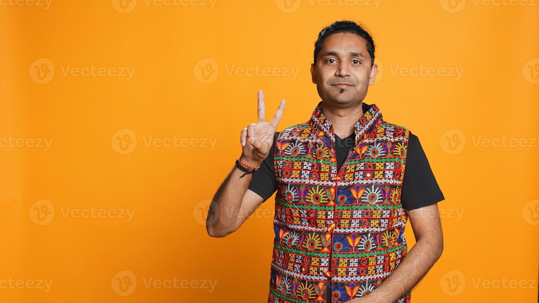 Portrait of upbeat man crossing fingers to make wish, hoping for good luck, isolated over studio background. Jolly indian person doing peace victory hand sign gesture, camera B photo