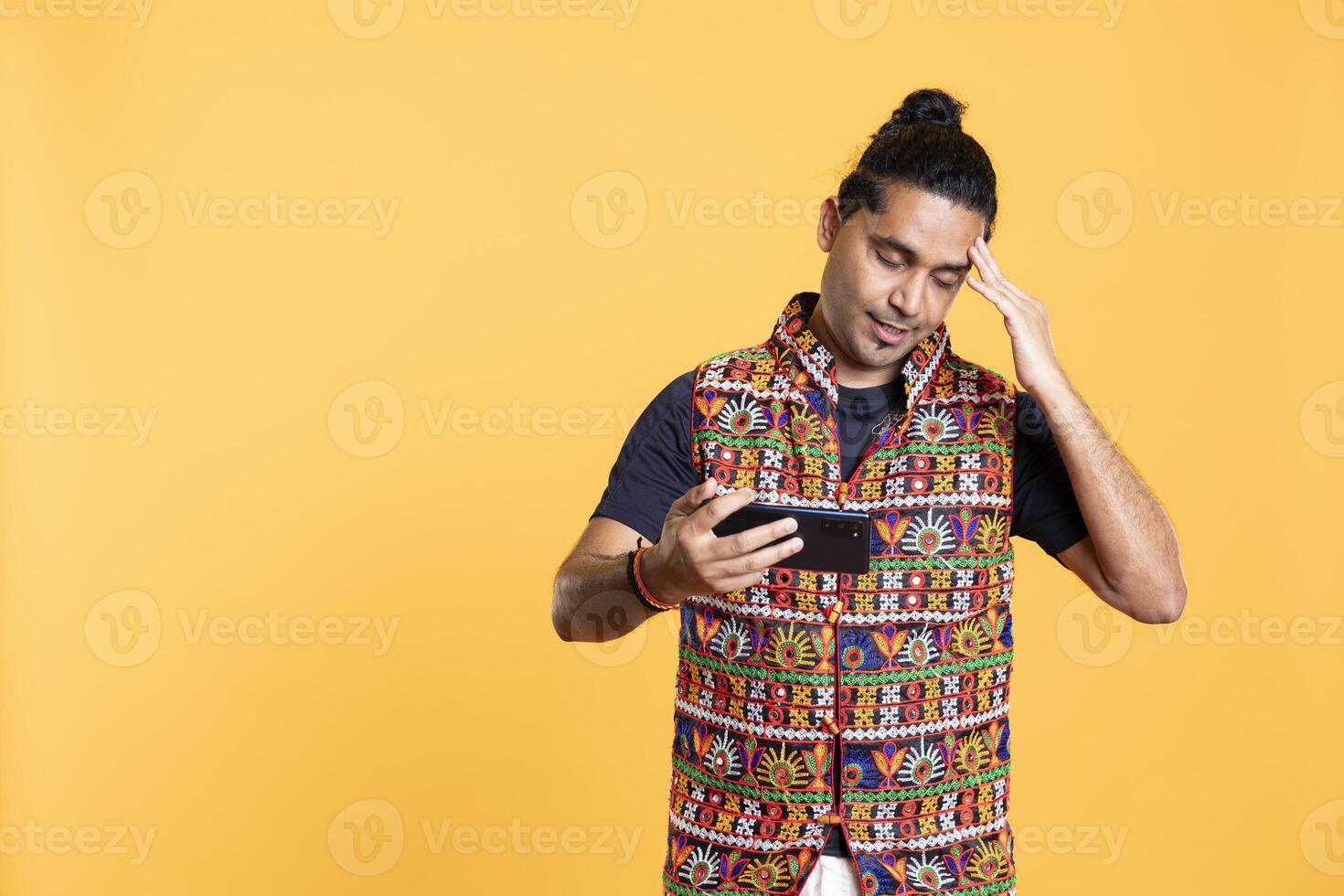 Gamer annoyed after losing online multiplayer videogame, being defeated by rival players. Indian man shocked and gutted after seeing game over message, holding phone, studio background photo
