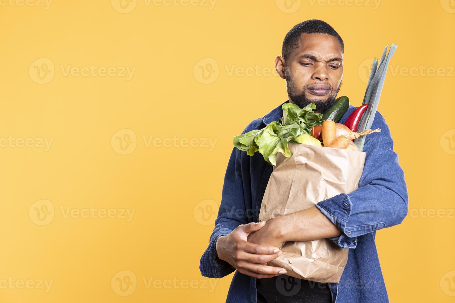 Pensive young man thinks of a food recipe with the organic ingredients he has, looking to make a delicious dinner with ethically sourced bio produce. African american guy prepares to cook. photo