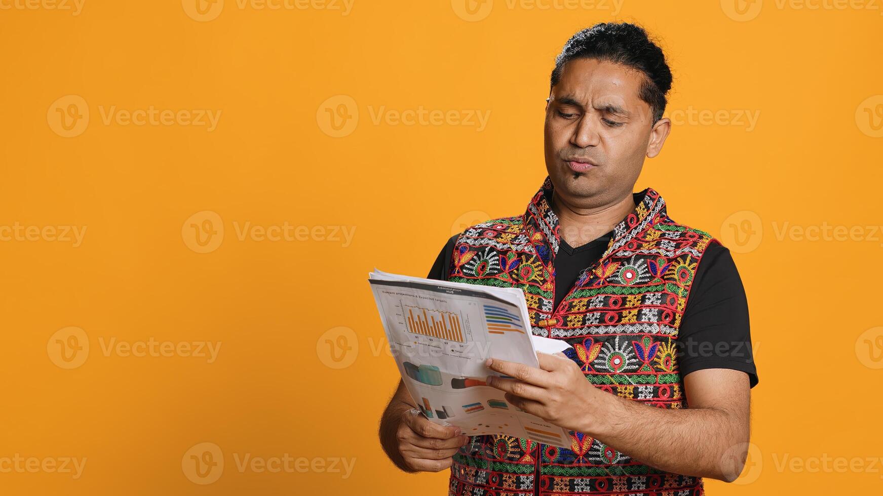 Man browsing though financial audit report files, slapping them in anger, disappointed by results, studio background. Upset indian worker frowning, annoyed by paperwork, camera A photo